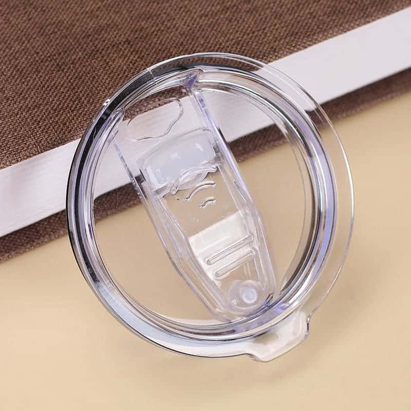 A macro overhead shot of a clear AS plastic splash-proof tumbler lid with a smooth transparent sliding toggle button on a book.