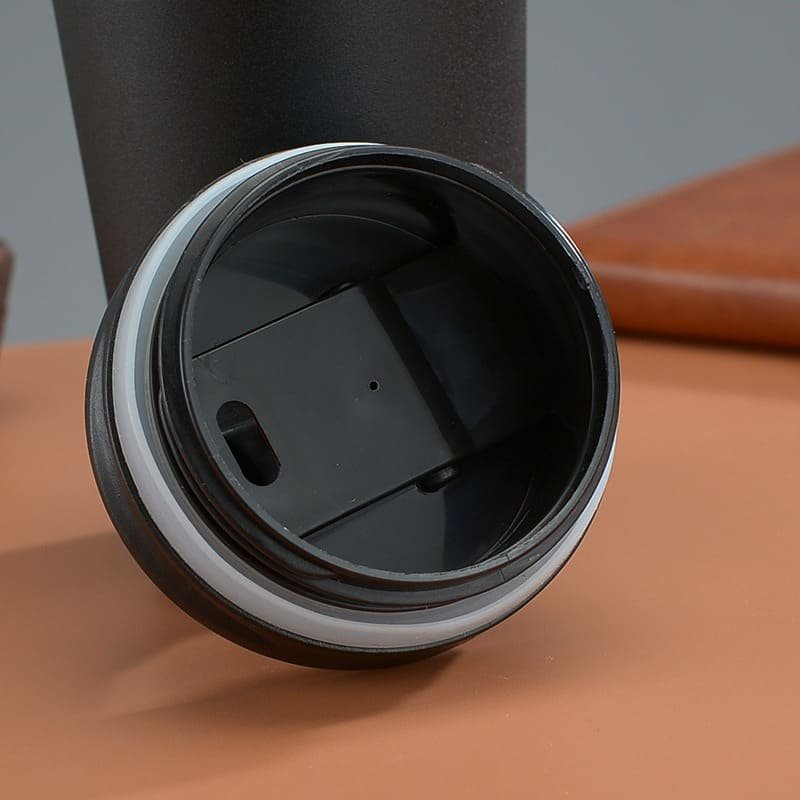 A detailed close-up shot under the black plastic flip lid of an insulated travel mug showing the thick white silicone sealing ring.