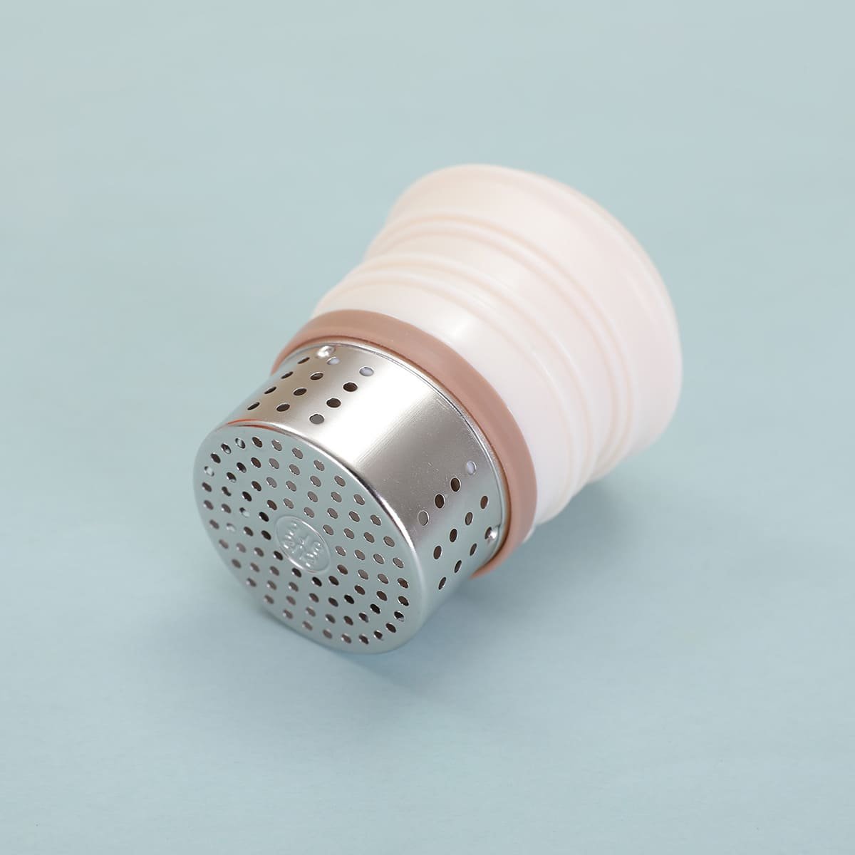 Isolated close-up of a precision-perforated stainless steel tea infuser stopper with a thick silicone sealing ring core for high-pressure thermal steeping.