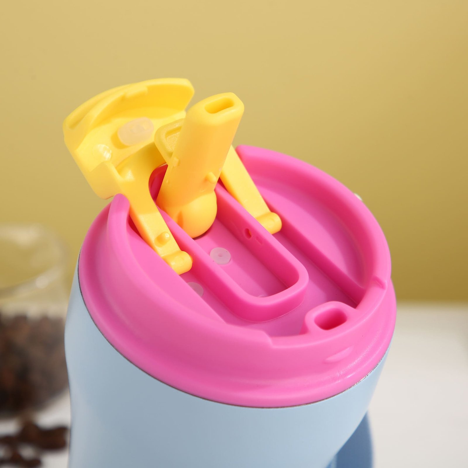 Close up top view of a colorful pink and yellow travel mug flip lid revealing the built-in soft silicone straw mouthpiece.