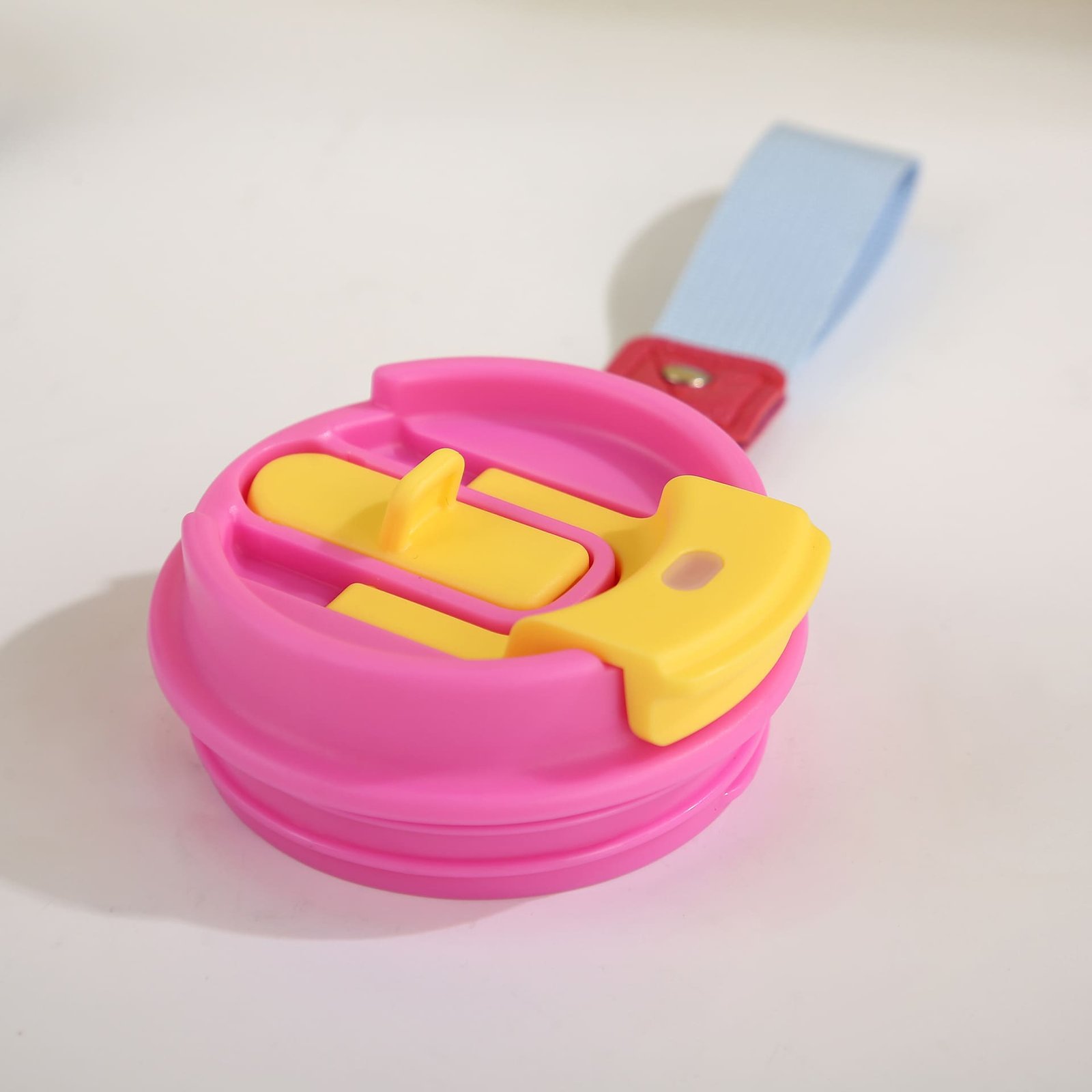 Detached pink and yellow flip cap for a coffee tumbler shown with a light blue heavy duty textile wrist strap.